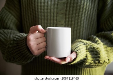 female hand holding white mug with blank copy space for your advertising text message or promotional content, sweet coffee or tea. Girl in green sweater holding white porcelain mug mock up - Shutterstock ID 2087119465