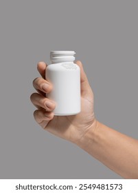 Female hand holding a white plastic pill bottle closeup against grey background.  Packaging mockup for your pills or capsules herbal supplement