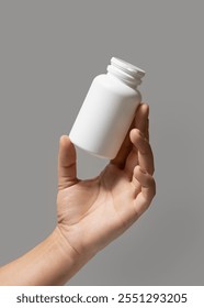 Female hand holding a white plastic pill bottle closeup against grey background.  Packaging mockup for your pills or capsules herbal supplement