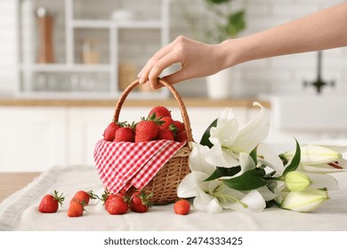 Female hand holding wicker basket with tasty strawberries and lily flowers on table in kitchen - Powered by Shutterstock