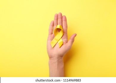 Female hand holding yellow ribbon on color background. Cancer concept