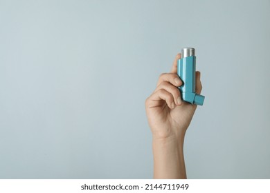 Female Hand Holds Asthma Inhaler On Light Gray Background