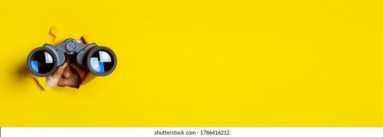 La mano femenina sostiene binoculares negros sobre un fondo amarillo. Viaje, búsqueda y concepto. Cartel.