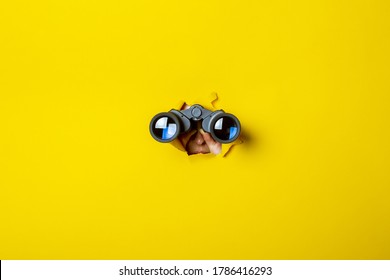 Female hand holds black binoculars on a yellow background. Journey, find and search concept