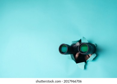 Female hand holds black binoculars on a blue background. Journey, find and search concept. Banner.