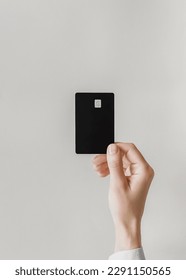 female hand holds a black plastic bank card on a gray background