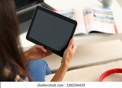 Female hand holds black tablet pad in home setting while sitting on couch engaged an blogger surfing using application mail tracking food delivery display leisure listering music concept closeup.