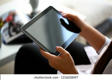 Female hand holds black tablet pad in home setting while sitting on couch engaged an internet surfing using application mail tracking food delivery display leisure listering music concept closeup.