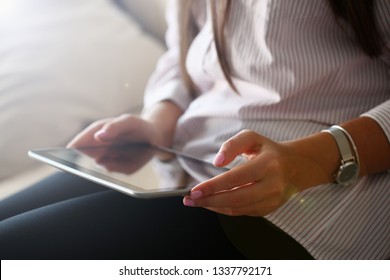 Female hand holds black tablet pad in home setting while sitting on couch engaged an internet surfing using application mail tracking food delivery display leisure listering music concept closeup.