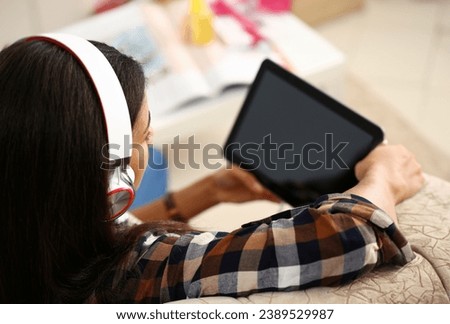 Female hand holds black tablet pad in home setting while sitting on couch engaged an internet surfing using application. Mail tracking food delivery display leisure listering music concept closeup.