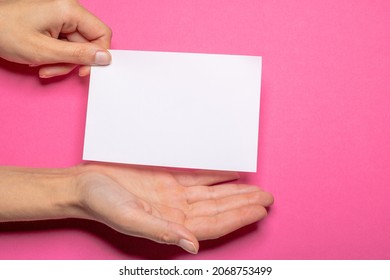 Die weibliche Hand hält ein leeres Stück Papier mit Kopienraum vor einem hellrosa Hintergrund-Karton, bei dem die Hand eine Geste macht