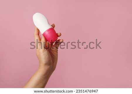Female hand holds body deodorant on pink background, copy space