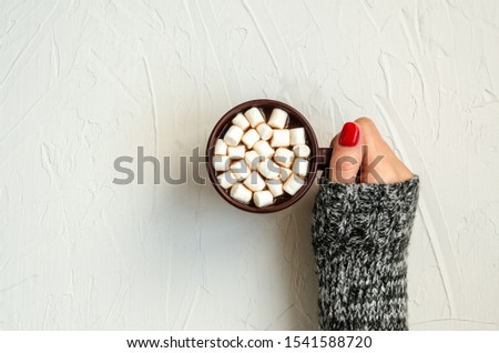 Female hand holds a brown cup with hot cocoa with white marshmallows on a white background with space for copy. The concept of comfort, warmth. Top view, close-up, flat lay.
