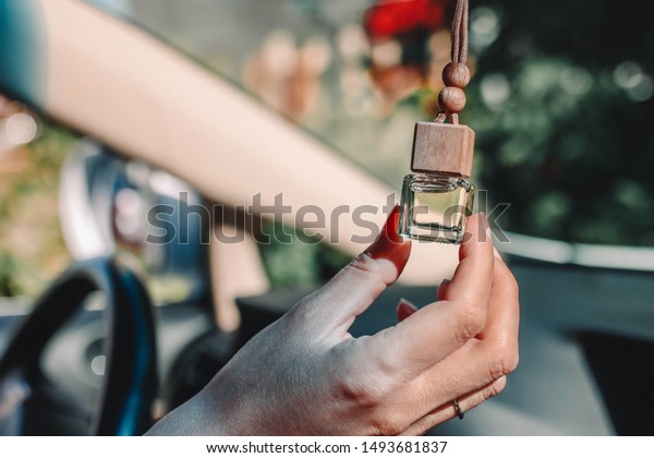 Female hand holds car air freshener.\
Small glass bottle with car perfume hanging in the\
car.