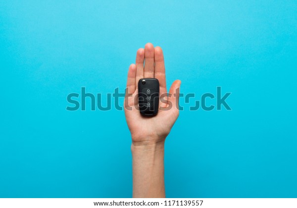 Female hand holds a car key in the palm on a blue\
background. Co
