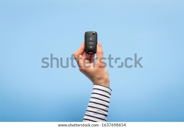 Female hand holds car keys on a blue background.\
Concept car, car rental, gift, driving lessons, driving license.\
Banner. Flat lay, top\
view