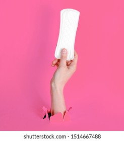 Female Hand Holds Daily Sanitary Pad Through Torn Pink Paper Background. Minimalistic Fashion Concept