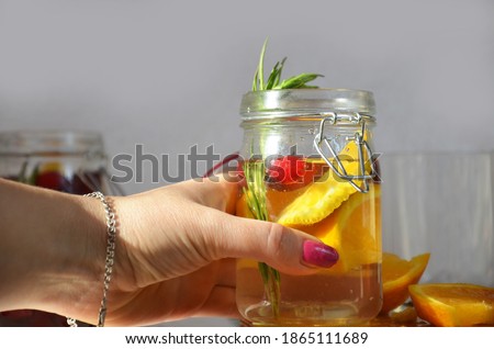 female hand holds detox water with orange, cranberry and rosemary, healthy drink for the diet, vitamin C. Festive cranberry citrus cocktail. Top view, space for text.