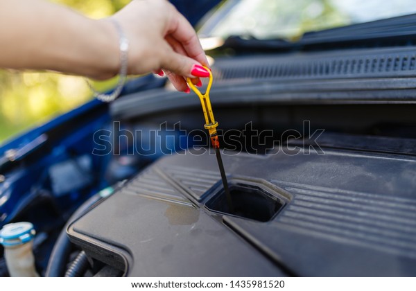 The female hand holds the dipstick oil level in\
the engine. Close-Up Of Woman Checking Car Engine Oil Level On\
Dipstick. Engine oil level\
testing