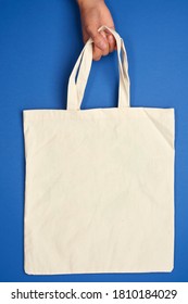 female hand holds an empty beige textile bag by the handles on a blue background, rejection of plastic bags, zero waste  - Shutterstock ID 1810184029