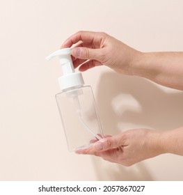 Female Hand Holds Empty Plastic Container With Dispenser For Liquid Products, Soap Or Shampoo On Beige Background