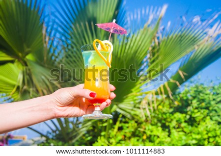 Female hand holds an exotic cocktail on the background of a palm