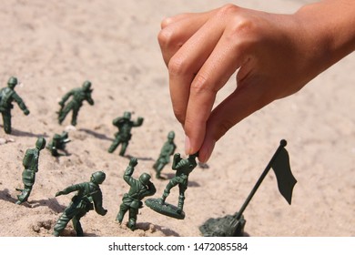 A female hand holds the green figure of a military soldier by the head. Other figures are arranged around in the sand. The concept of strategy and military action. Toy war. - Powered by Shutterstock