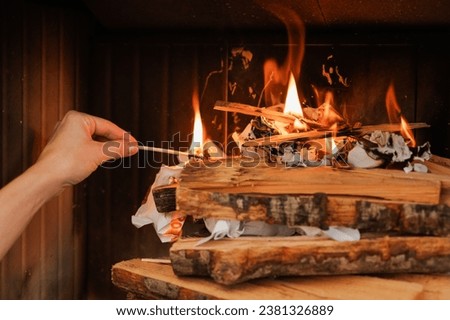 Female hand holds a matchstick, ready to ignite the firewood in a fireplace.