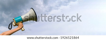 A female hand holds a megaphone. Horn loudspeaker is big and old. Clouds background. The concept of a message in business, loudspeaker, attracting attention.