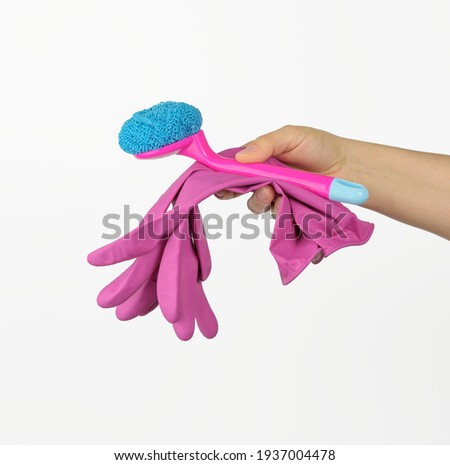 female hand holds pink cleaning gloves and a brush on a white background, close up