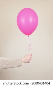 A female hand holds a pink helium balloon. The concept of holiday decorations, accessories for the children's holiday. Template for inserting your text. Minimalism, vertical image