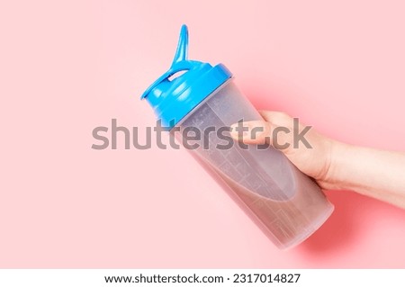 Female hand holds a shaker with protein shake on a pink background.