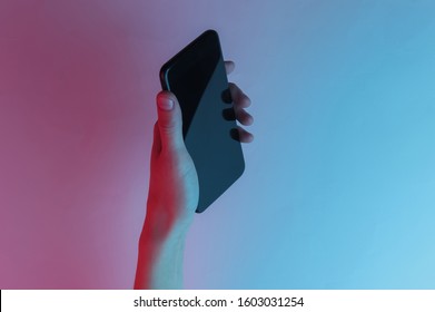 Female Hand Holds A Smartphone. Creative Pop Art Pink Blue Neon Color. Trendy Gradient Illumination. Night Light