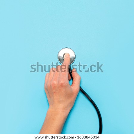 Female hand holds a stethoscope on a blue background. Concept doctor, doctor's appointment, virus, treatment, diagnosis. Flat lay, top view