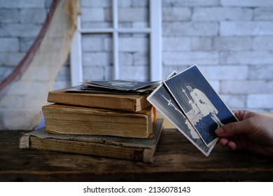 Female Hand Holds Vintage Photos, Retro Photography Of 1940-1950 On Wooden Table, Old Books, Concept Of Genealogy, Memory Of Ancestors, Family Tree, Genealogy, Childhood Memories, Family Archive