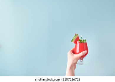 Female hand holds watermelon cocktail in glass with mint and ice on blue background. Colorful hot summer holidays. Close up slices of watermelon in hands. Banner. Mock up.