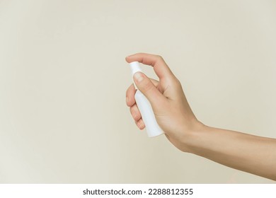 female hand holds a white spray bottle on a gray background. liquid products in spray bottles