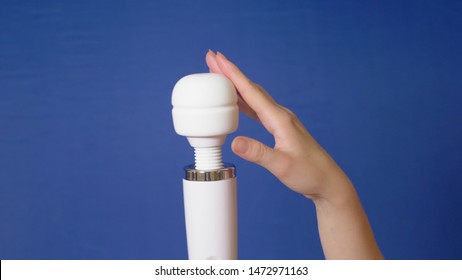 female hand holds a white vibrator on a blue background. copy space