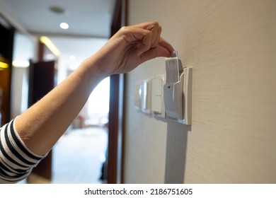 Female Hand Insert Key Card In In Holder On Hotel Room Wall.