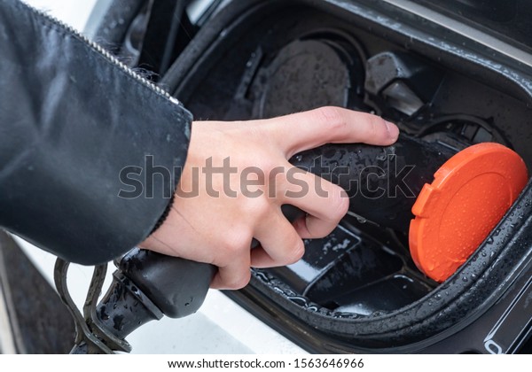 Female hand inserting\
charger plugs into an electric car. New energy vehicle, NEV is\
being loaded with electricity power. Ecology, modern-day cars,\
e-mobility.
