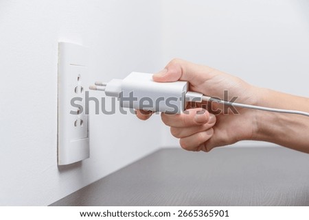 Female hand inserting a white electrical plug into outlet. Closeup view of a fork and a socket.