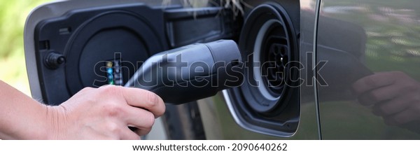 Female hand inserts plug for charging electric\
car closeup