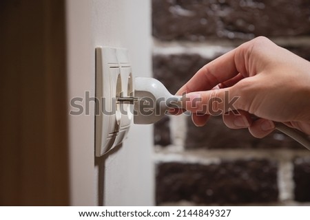 A female hand inserts white electric plug into a euro-format socket close-up