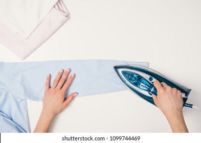 Female hand ironing clothes top view isolated on white background. Young woman with iron ironing shirt seen from above during housework. Blue iron isolated on white table.