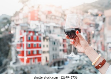 Female Hand With Italian Flag Nail Art Holding Glass With Red Wine On A Background Of Cinque Terre Riomaggiore Town