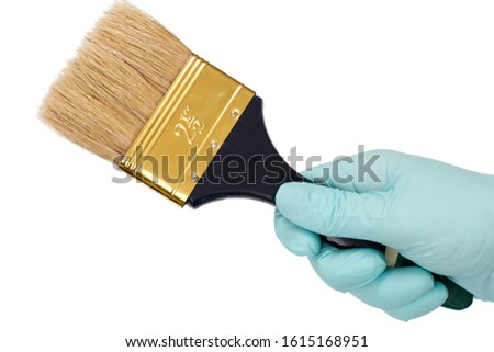 Female hand in a latex glove holding a house painter brush on a white isolated background. Repair tool. Building tool. Close-up view.