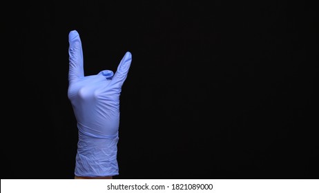 Female Hand In A Latex Medical Glove Makes An Rock Gesture Isolated On Black Background.