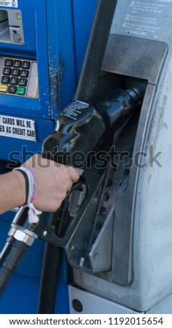Female hand lift fuel nozzle at gas station pump to fill car gasoline tank with high octane grade for power to drive automobile