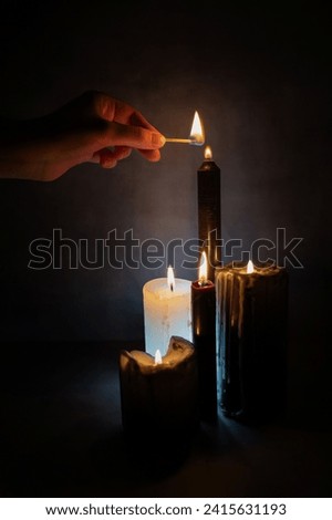 Female hand lighting black candles for a magical ritual, Halloween or occultism, mystical.
