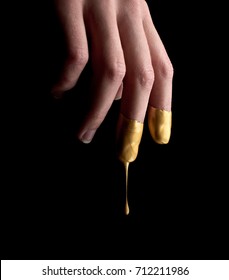 Female hand in liquid gold, drops drip from fingers, on a black background